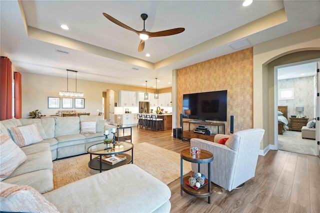 living room with hardwood / wood-style flooring, ceiling fan, and a tray ceiling