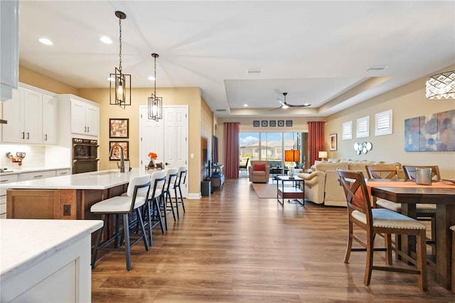 kitchen featuring dark wood-type flooring, a kitchen bar, white cabinetry, hanging light fixtures, and a kitchen island with sink