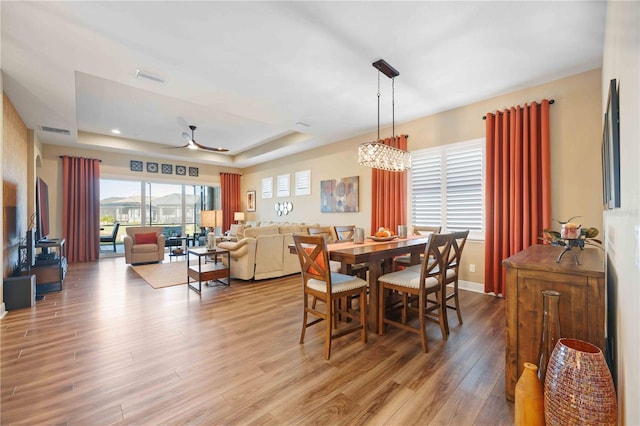 dining room featuring ceiling fan with notable chandelier, light wood-type flooring, and a tray ceiling