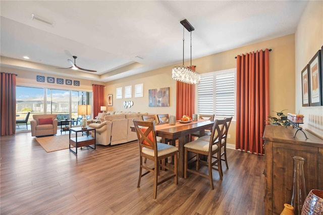 dining room featuring wood-type flooring, ceiling fan with notable chandelier, and a tray ceiling