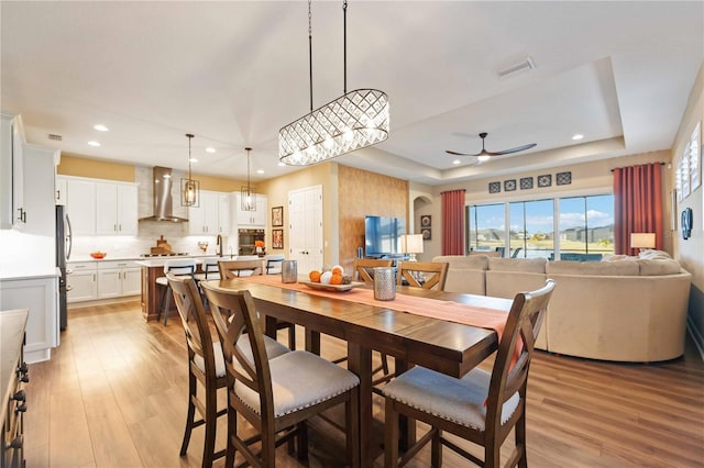 dining room featuring ceiling fan, a raised ceiling, and light hardwood / wood-style flooring