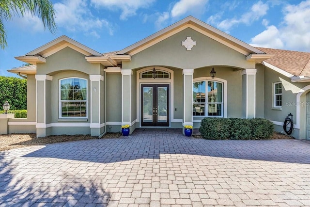 property entrance with french doors, a shingled roof, and stucco siding