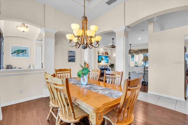 dining room featuring arched walkways, hardwood / wood-style flooring, decorative columns, visible vents, and ceiling fan with notable chandelier