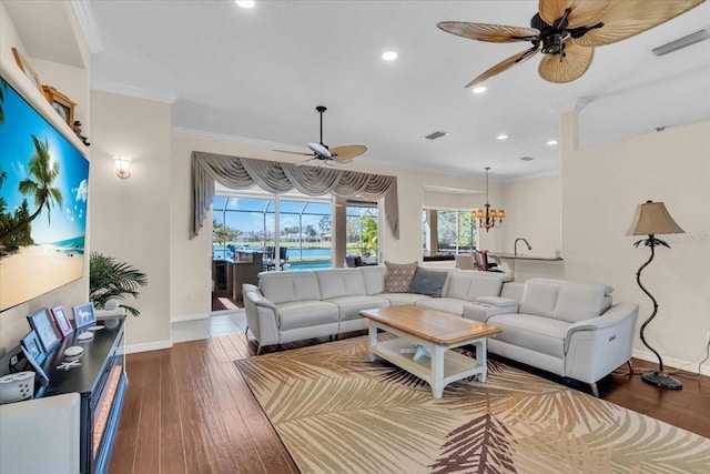 living area with ceiling fan with notable chandelier, wood-type flooring, visible vents, and crown molding