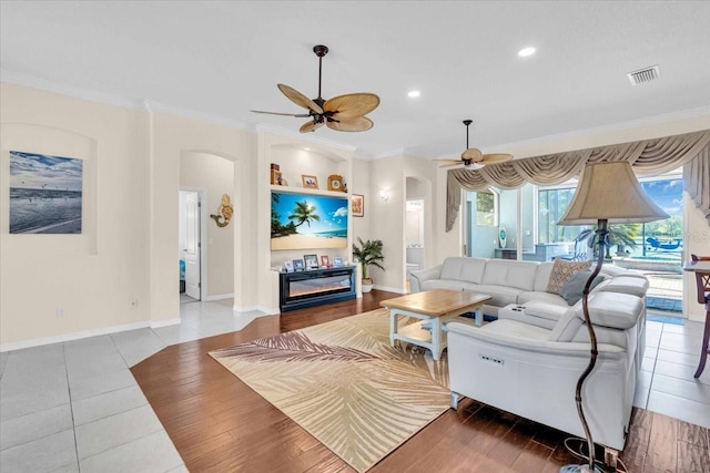 living area with ornamental molding, a glass covered fireplace, arched walkways, and wood finished floors