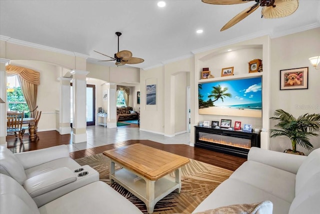 living room with arched walkways, a ceiling fan, a glass covered fireplace, wood finished floors, and a wealth of natural light