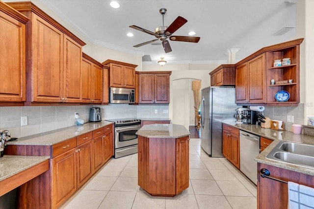 kitchen with light tile patterned floors, brown cabinetry, a kitchen island, stainless steel appliances, and crown molding