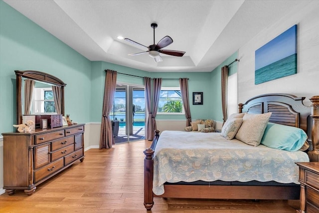 bedroom featuring light wood-style floors, access to outside, a raised ceiling, and multiple windows