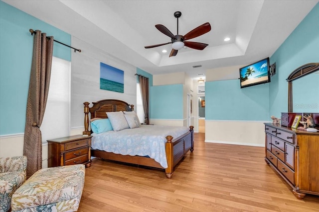 bedroom with light wood finished floors, baseboards, a raised ceiling, and recessed lighting