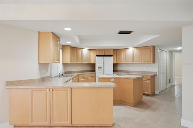 kitchen featuring sink, a tray ceiling, white refrigerator with ice dispenser, light brown cabinetry, and kitchen peninsula