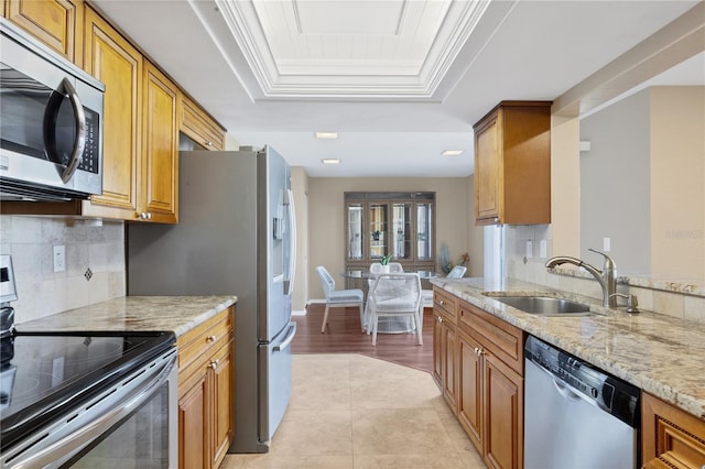 kitchen featuring appliances with stainless steel finishes, sink, decorative backsplash, a tray ceiling, and light stone countertops