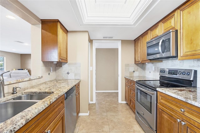 kitchen with sink, light tile patterned floors, a tray ceiling, stainless steel appliances, and light stone countertops