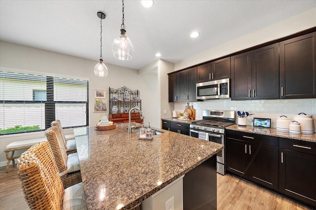 kitchen featuring dark brown cabinetry, sink, stone countertops, hanging light fixtures, and appliances with stainless steel finishes