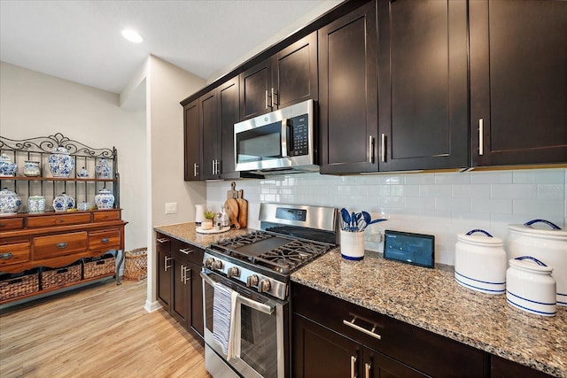 kitchen with dark brown cabinetry, tasteful backsplash, light wood-type flooring, stainless steel appliances, and light stone countertops