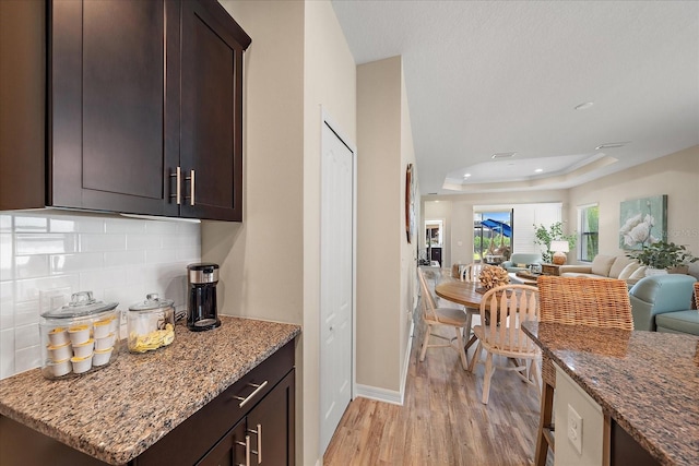 kitchen featuring light stone counters, backsplash, a tray ceiling, and light hardwood / wood-style floors