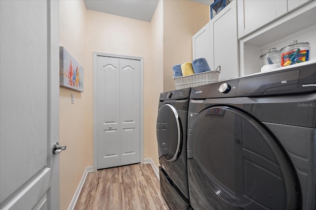 clothes washing area featuring cabinets, washer and dryer, and light wood-type flooring