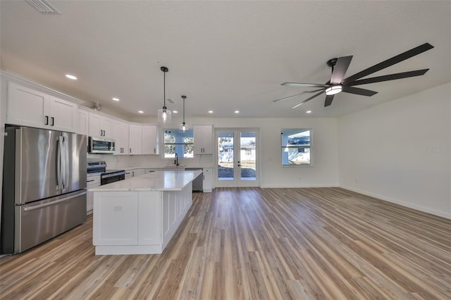 kitchen with a kitchen island, white cabinetry, sink, hanging light fixtures, and stainless steel appliances