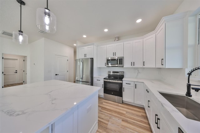 kitchen with white cabinetry, stainless steel appliances, sink, and pendant lighting