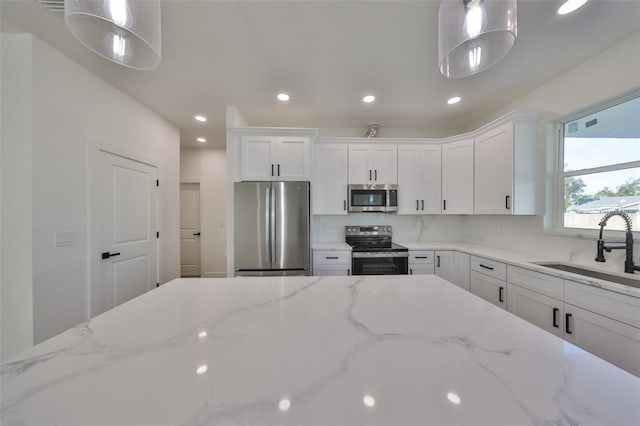 kitchen featuring sink, white cabinetry, hanging light fixtures, stainless steel appliances, and light stone countertops