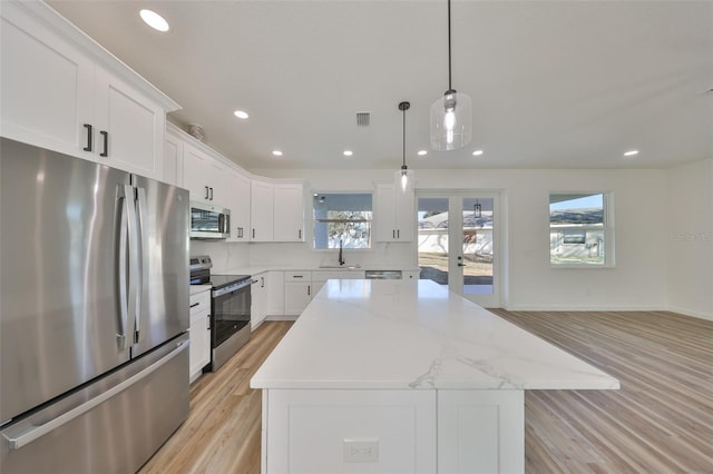 kitchen with sink, hanging light fixtures, a kitchen island, stainless steel appliances, and white cabinets