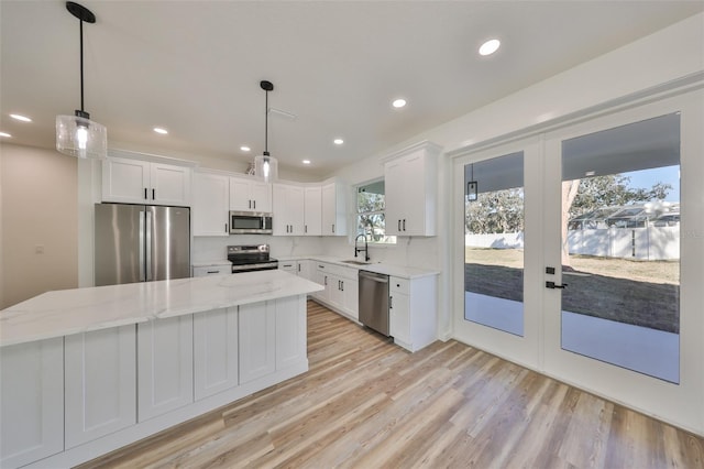 kitchen with sink, appliances with stainless steel finishes, a center island, white cabinets, and decorative light fixtures