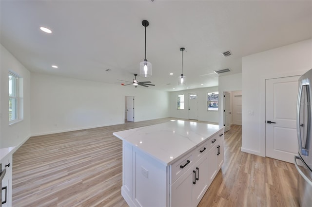 kitchen with a kitchen island, pendant lighting, white cabinets, light stone counters, and light wood-type flooring