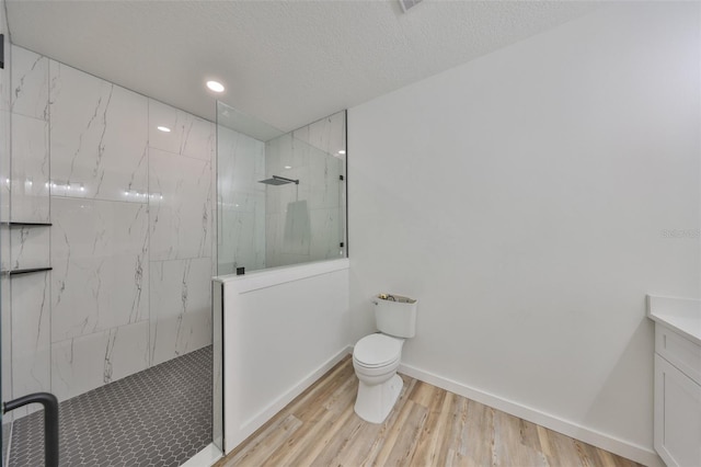 bathroom featuring hardwood / wood-style floors, tiled shower, vanity, a textured ceiling, and toilet