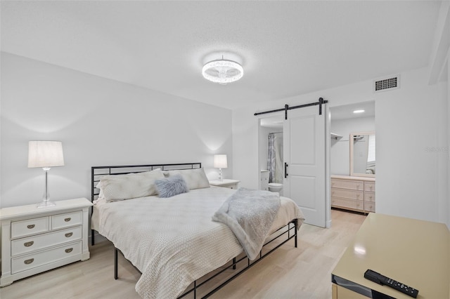 bedroom with ensuite bath, a barn door, and light wood-type flooring