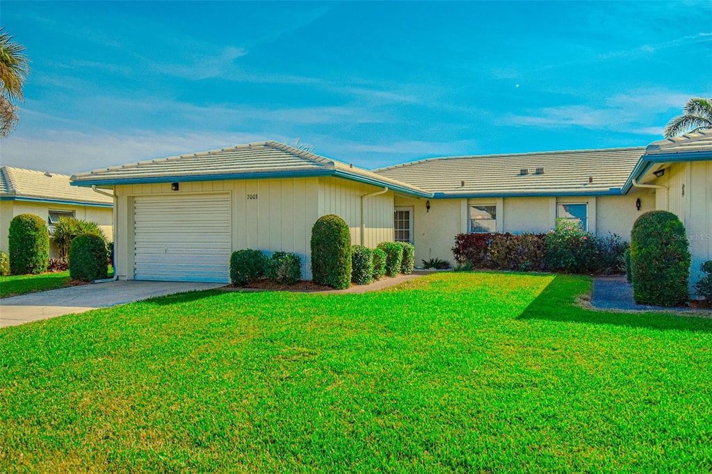 ranch-style house featuring a front yard, a tile roof, driveway, and an attached garage