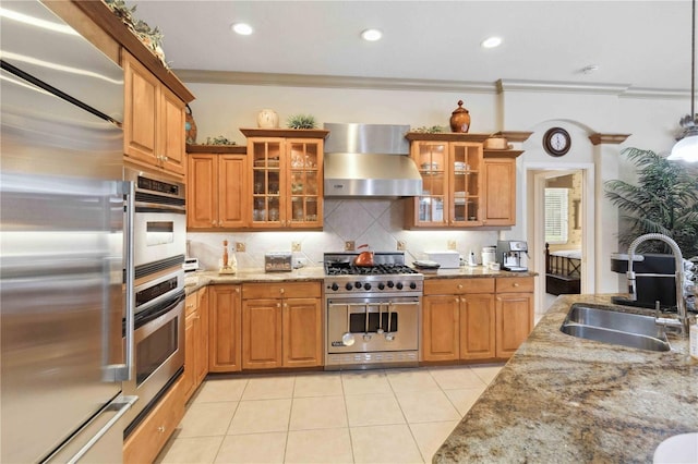 kitchen with high quality appliances, sink, light stone counters, and wall chimney exhaust hood