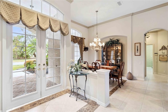 entryway with an inviting chandelier, a towering ceiling, ornamental molding, and light tile patterned floors