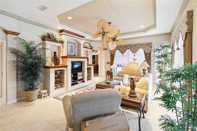 living room with ceiling fan, ornamental molding, a raised ceiling, and light tile patterned floors