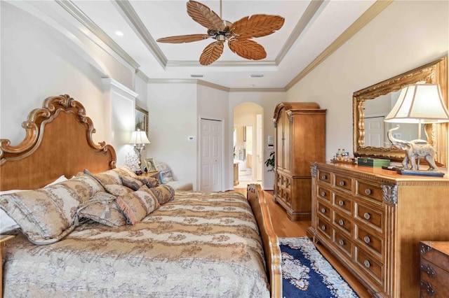 bedroom with ensuite bath, ornamental molding, a tray ceiling, hardwood / wood-style flooring, and ceiling fan