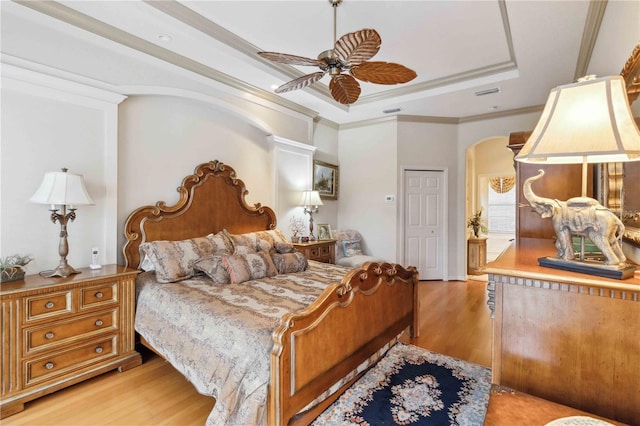 bedroom featuring crown molding, ceiling fan, a tray ceiling, and light wood-type flooring