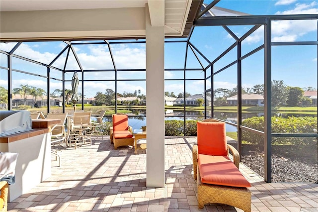 view of patio featuring exterior kitchen, a water view, and glass enclosure