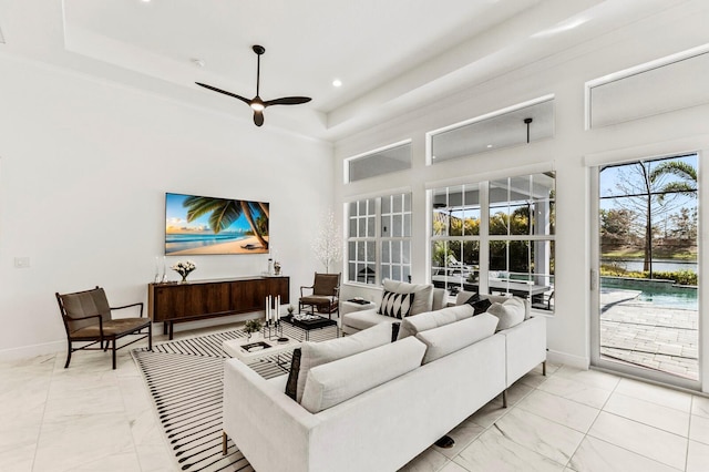 living room featuring a raised ceiling, ceiling fan, and a high ceiling