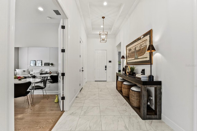 foyer with a high ceiling, crown molding, a raised ceiling, and a notable chandelier