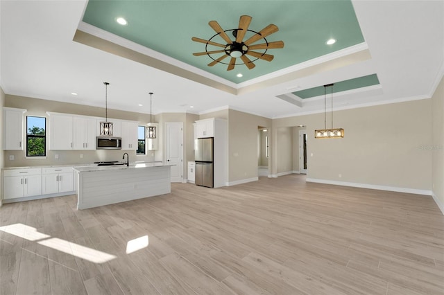 kitchen featuring pendant lighting, a kitchen island with sink, white cabinetry, stainless steel appliances, and a raised ceiling