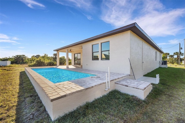 view of swimming pool with cooling unit, ceiling fan, a patio area, and a lawn