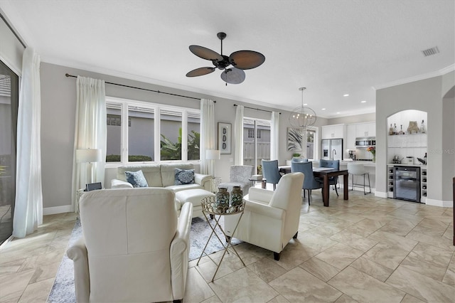 living room with wine cooler, ornamental molding, and ceiling fan with notable chandelier