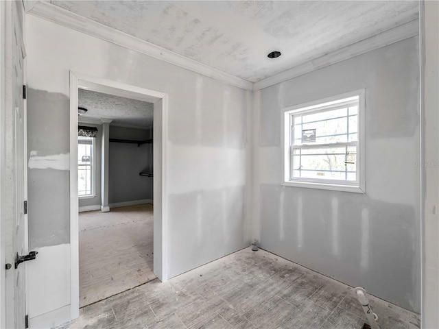 spare room with crown molding, a textured ceiling, and light wood-type flooring