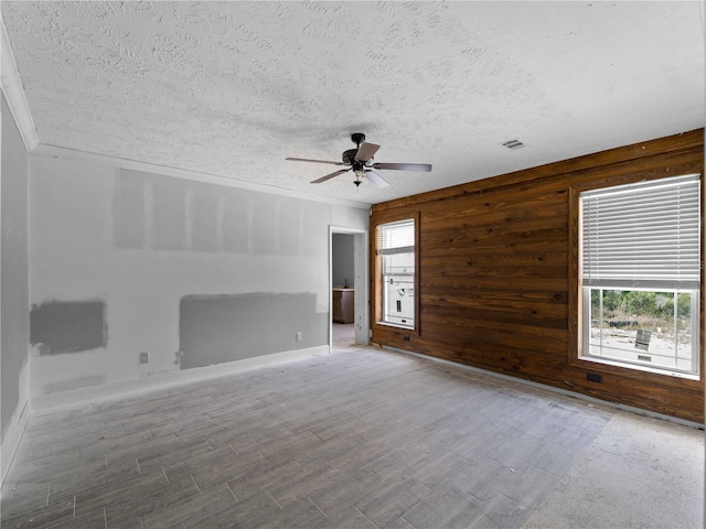 unfurnished room featuring ceiling fan, ornamental molding, a textured ceiling, and wood walls