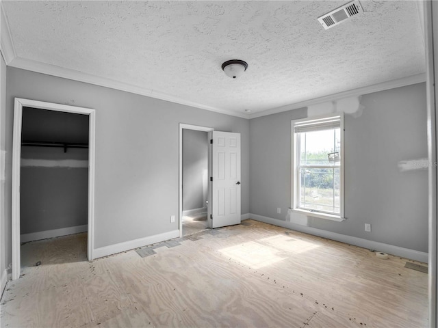 unfurnished bedroom featuring a spacious closet, ornamental molding, a closet, and a textured ceiling