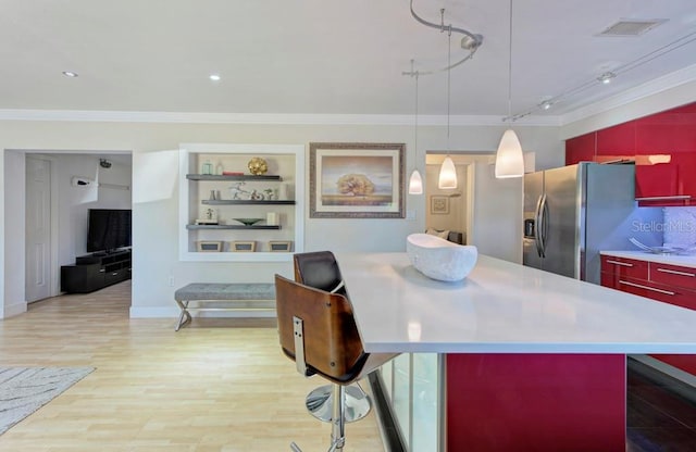 kitchen with visible vents, ornamental molding, light wood-type flooring, stainless steel fridge, and a kitchen breakfast bar