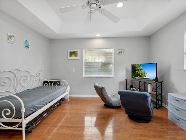 bedroom with light hardwood / wood-style flooring, a raised ceiling, and ceiling fan
