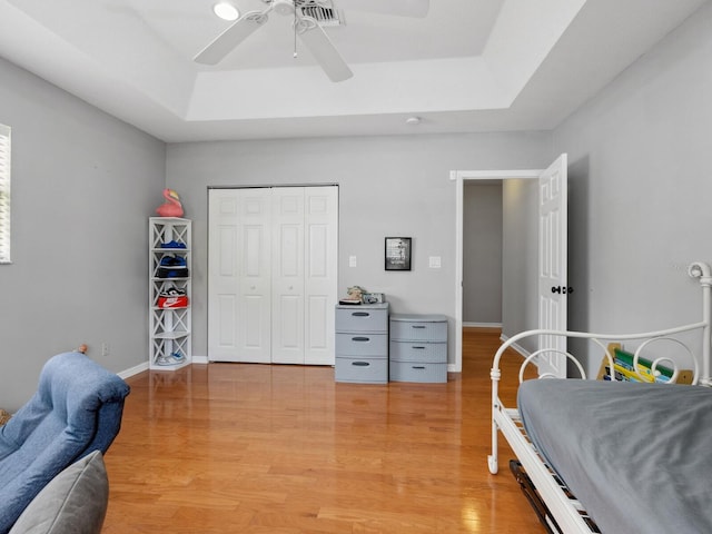 bedroom with ceiling fan, a tray ceiling, hardwood / wood-style floors, and a closet
