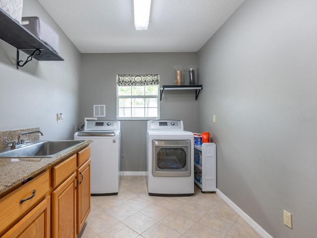 washroom with sink, a textured ceiling, cabinets, and washing machine and clothes dryer