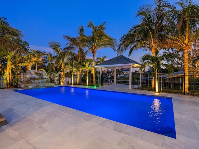 pool at dusk featuring a gazebo, pool water feature, and a patio