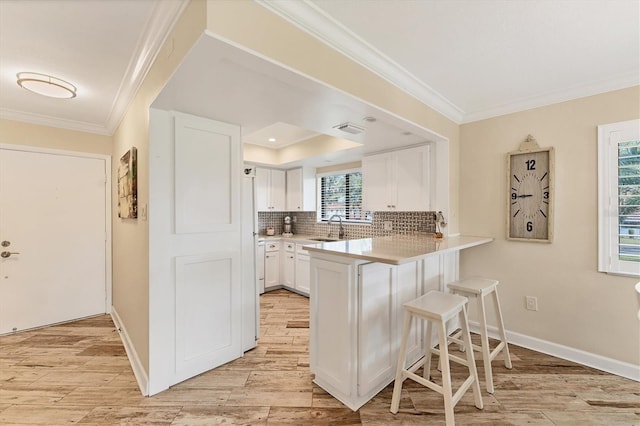 kitchen featuring sink, white cabinetry, tasteful backsplash, light wood-type flooring, and kitchen peninsula