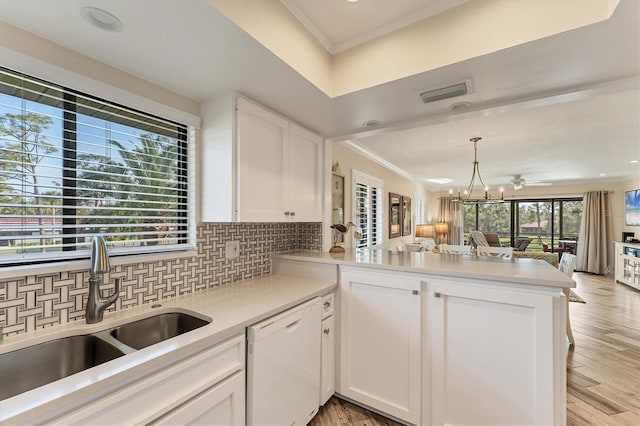 kitchen with sink, white dishwasher, ornamental molding, white cabinets, and kitchen peninsula